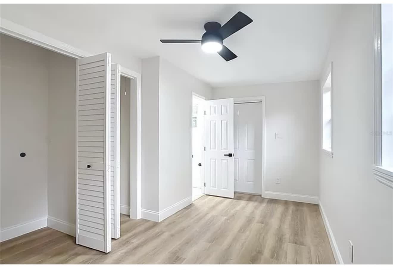 Remodeled bedroom with louvered closet doors, wood-look flooring, and ceiling fan, first angle