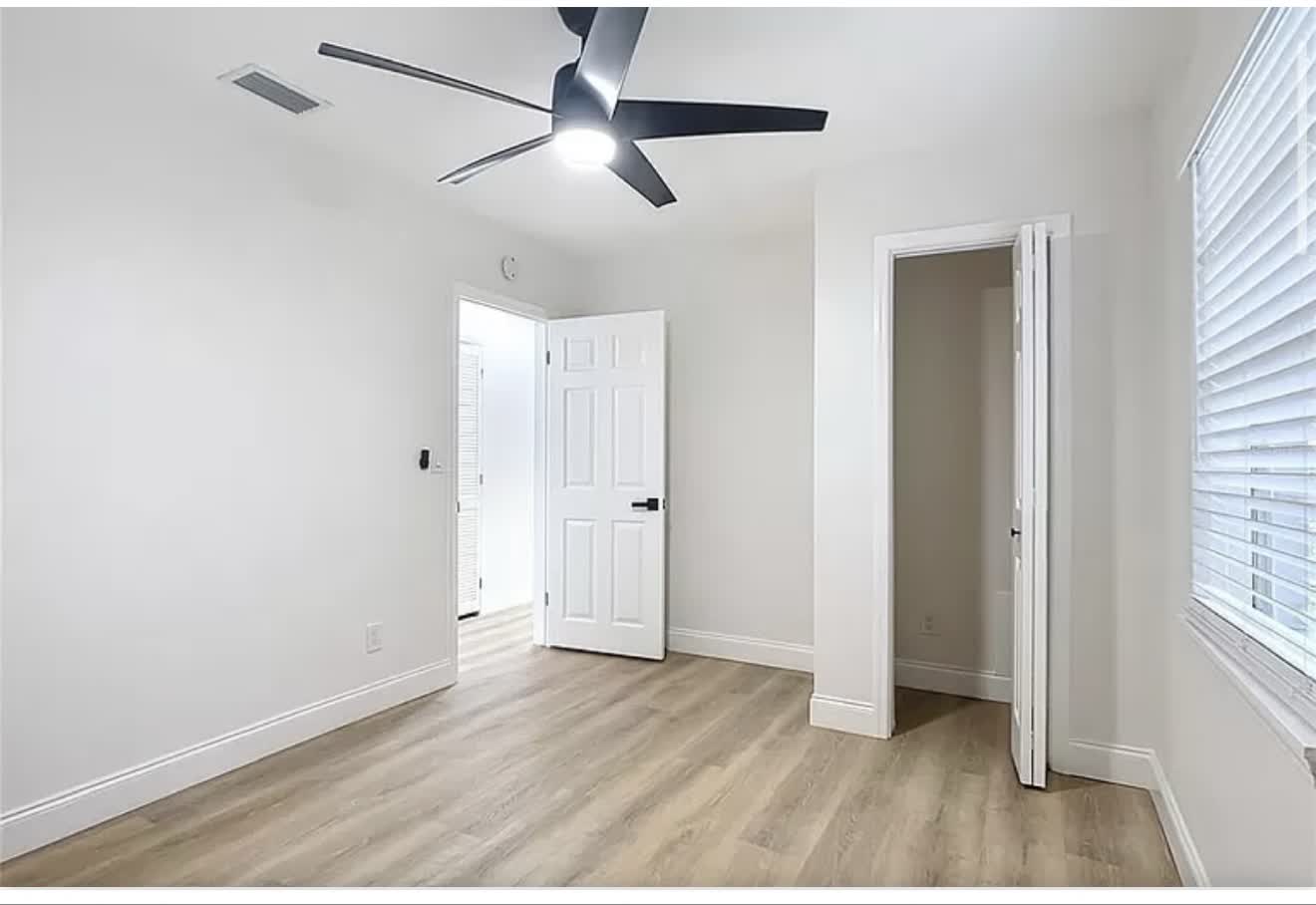 Remodeled bedroom with louvered closet doors, wood-look flooring, and ceiling fan, second angle