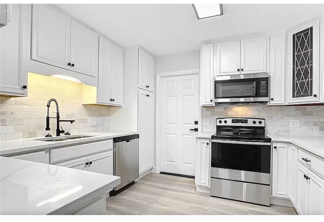 Remodeled kitchen with white shaker cabinets, stone-look counters, sink, and faucet