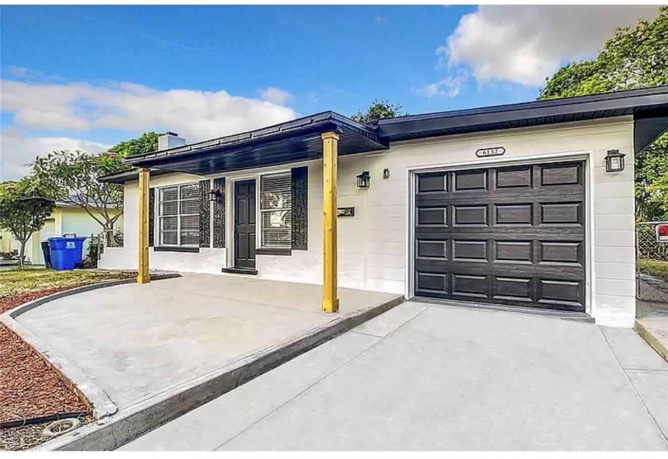 Remodeled house exterior from the side with white paint and black garage door, first angle